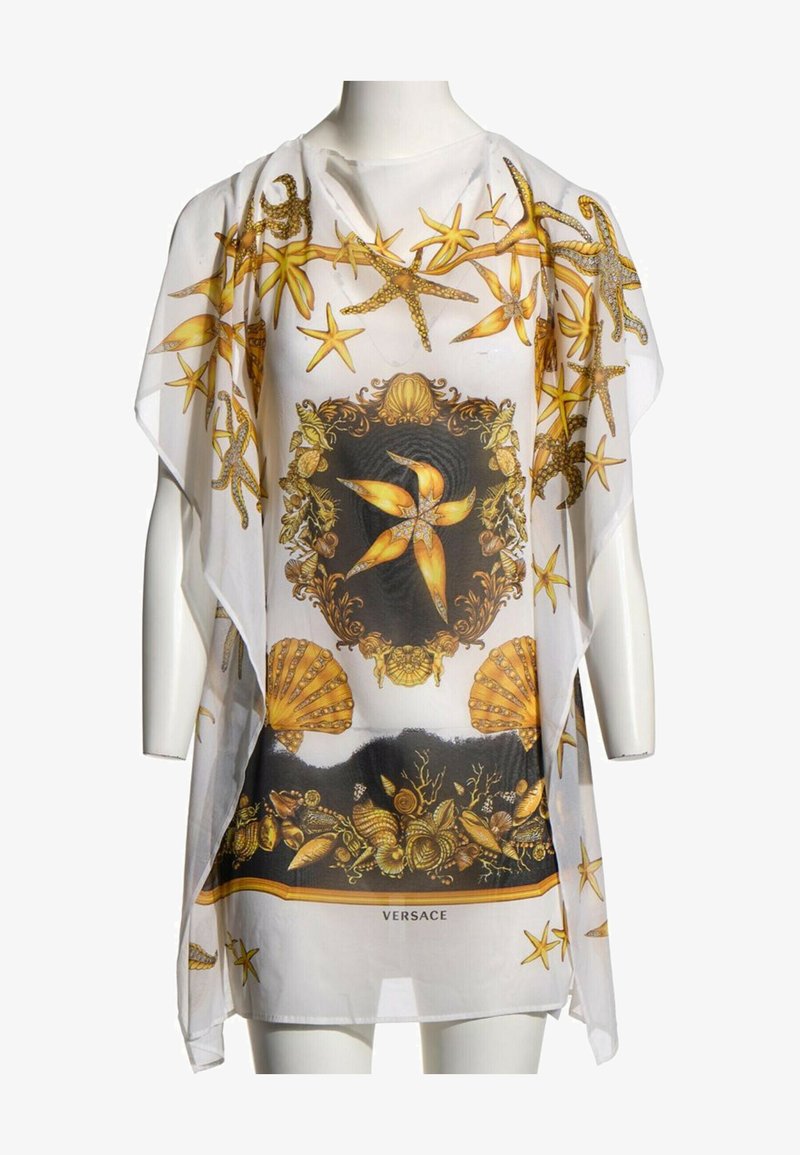 Tunique blanche transparente avec des étoiles de mer dorées, des coquillages et des motifs marins ornés, avec le logo Versace en bas au centre.
