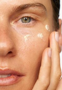 Gros plan sur une peau appliquant une crème. La texture est crémeuse et légère, de couleur claire, sur une surface de peau lisse et légèrement tachetée de roux.