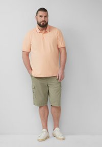Hellrosa Polohemd mit Kragen und kurzen Ärmeln, kombiniert mit olivgrünen Cargo-Shorts und weißen Sneakers. Einfaches Design, lässiger Look.