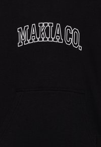 Svart genser med "MAKIA CO." i hvite, buede bokstaver. Har en frontlomme og et mykt, strukturert stoff.
