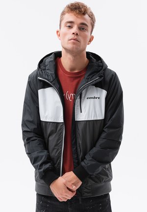 Svart och grå sportjacka med huva, med en frontdragkedja och tvåfärgad design, texturerad tyg och "ombre"-logga på bröstet.