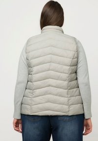 Jasnoszary puchowy kamizelka z przeszyciami w kształcie zygzaka, dopasowanym kołnierzem i odpinanymi rękawami. Pod nią znajduje się długorękawowa szara bluzka.