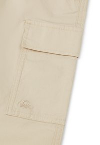 Beige Cargo-Hosen mit einer Seitentasche, verstärkten Nähten und einem dezenten gestickten Logo in der Nähe der Tasche. Glatte Textur.