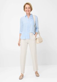 Hellblaues Leinenhemd mit Knöpfen kombiniert mit beigen, gemusterten Hosen. Das Outfit umfasst weiche beigen Slipper und eine kleine Umhängetasche.