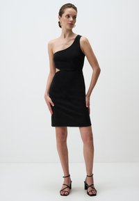 Schwarzes einseitiges Kleid mit tailliertem Design, Ausschnitt in der Taille und glatter Textur. Kombiniert mit schwarzen Riemchenheels.