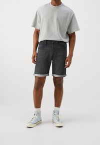 Grå T-shirt, mörka denimshorts med uppvikta ben, och ljusblå högskurna sneakers. Avslappnad, enkel design med minimala detaljer.