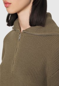 Khaki Reißverschluss-Pullover aus strukturiertem Strick mit hohem Kragen und silbernem Reißverschluss, zu sehen vom Nacken- bis zum Schulterbereich.