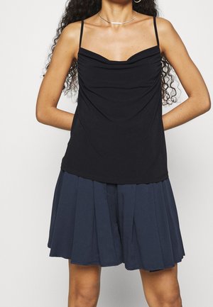 Czarny top z golfem na cienkich ramiączkach, w zestawieniu z granatową plisowaną spódnicą. Gładka tkanina o luźnym kroju i subtelnie opadająca na torsie.