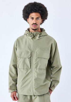 Chaqueta con capucha de color verde oliva claro, hecha de tela texturizada, con dos grandes bolsillos en el pecho y puños ajustables. Diseño simple con un mínimo de marca.