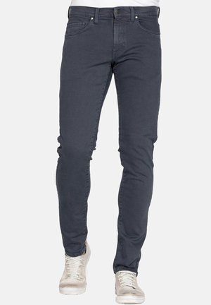 Jeans slim-fit grigio scuro con una texture liscia, tasche anteriori e posteriori, e chiusura classica con bottone, abbinati a sneaker chiare.