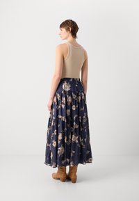 Beige tank topp kombinert med en marineblå blomstrete maxiskjørt, med lagdelte lag og lett materiale. Avsluttet med brune ankelstøvler.