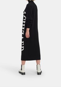 Svart stickad klänning med hög hals, med en stor vit grafik på sidan. Kombinerad med vita ankelstövlar och en texturerad sula.