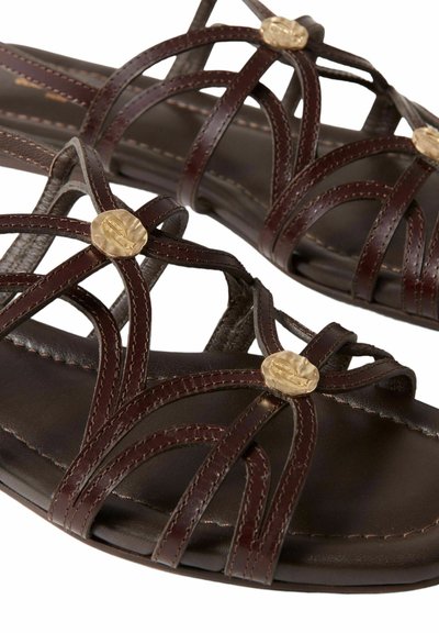 Sandali in pelle marrone con molteplici cinturini sottili e piccoli bottoni decorativi dorati ad ogni incrocio dei cinturini.