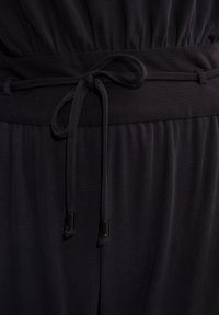 Czarny, prążkowany kombinezon z zebranym pasem i związanym paskiem. Gładka tekstura z metalowymi końcówkami na sznurkach.