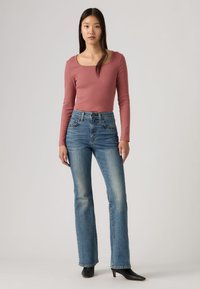 Μακρυμάνικο τοπ με στρογγυλή λαιμόκοψη σε ροζ απόχρωση, σε συνδυασμό με ψηλόμεσα τζιν παντελόνια με ίσια γραμμή και μαύρα παπούτσια μυτερά.