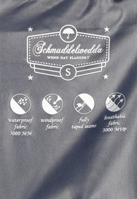 Szürke, sima textúrájú szövet fehér grafikával és szöveggel, amely a vízálló, szélálló és lélegző tulajdonságokat, valamint a teljesen ragasztott varrásokat emeli ki.