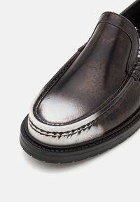 Chaussures plates en cuir noir et argenté avec une finition polie, des coutures contrastées et une semelle en caoutchouc robuste.