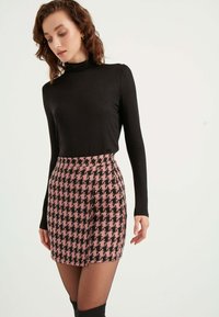 Schwarzer Rollkragenpullover kombiniert mit einem taillierten Rock aus Pink und Schwarz im Hahnentrittmuster, mit strukturierter Oberfläche und knielangem Schnitt.