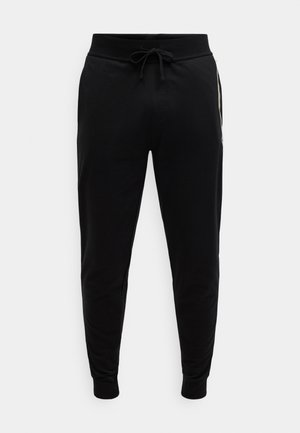 Μαύρο παντελόνι τζόγκινγκ από μαλακό βαμβάκι με ελαστική μέση και ρυθμιζόμενο κορδόνι· εφαρμοστά τελειώματα στους αστραγάλους· χωρίς ορατά σχέδια.