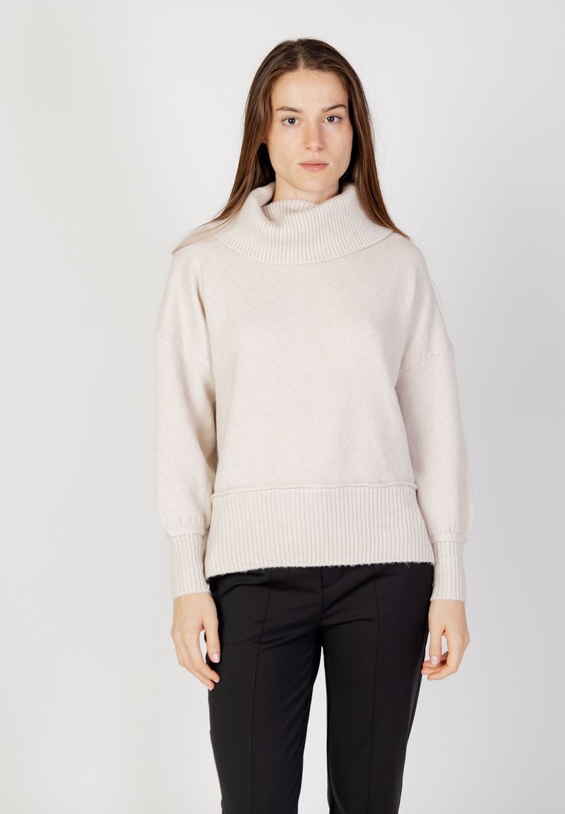 Beige polokrage tröja med ribbstickad struktur och mudd, med en lös passform och bred halsringning. Kombinerad med svarta åtsittande byxor.