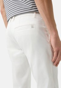 Witte katoenen broek met een achterzak met een subtiel 'B' logo, gecombineerd met een grijs-wit gestreept shirt. Een zachte textuur en een getailleerde pasvorm.