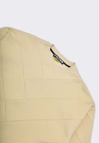 Felpa beige con pannelli texturizzati, scollo rotondo e polsini a costine. Presenta un'etichetta nera con logo bianco all'interno del collo.