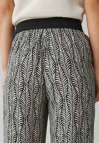 Zwart-wit gepatternde broek met een bladerenontwerp, voorzien van een brede elastische tailleband en een vloeiende stoftextuur.