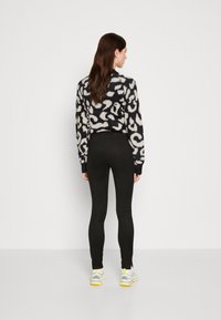 Black and cream patterned sweater with a fuzzy texture, paired with tight black leggings and white sneakers with yellow accents.
