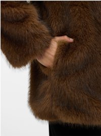 Ranka įdėta į storą rudą kailinį paltą, pabrėžianti audinio tekstūrą ir šilumą.