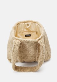 Beige pluchen draagtas met een zachte textuur, voorzien van twee handgrepen en een ritsvak aan de binnenzijde tegen een lichtgekleurde voering.