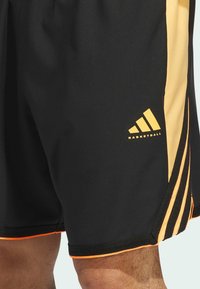 Pantalones cortos de baloncesto negros con acentos laterales amarillos, que presentan un logo y un ribete naranja. Fabricados con un tejido ligero y suave para mayor comodidad.