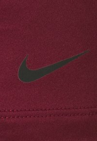 Logotipo negro de Nike Swoosh sobre tela texturizada roja con costuras visibles cerca del borde inferior.