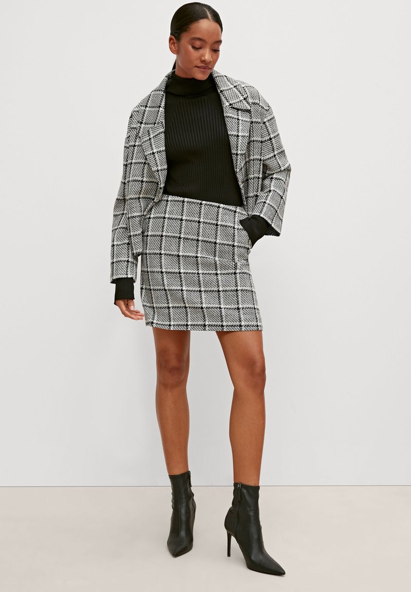 Black and white checked blazer, ribbed black turtleneck, matching miniskirt, and black ankle boots with a pointed toe and sleek design.