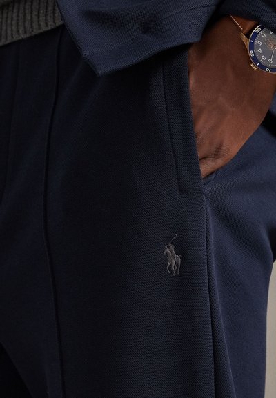 Μπλε ναυτικό τζόγκερ από υφασμάτινη υφή, με πλαϊνή τσέπη και μικρό γκρι λογότυπο πόλο στο αριστερό πόδι.