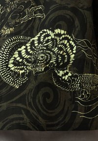 Black textile featuring intricate patterns of a tiger and dragon in gold and green. The design includes swirling elements and detailed textures.