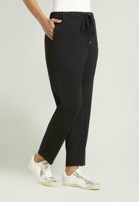 Pantalones jogger negros con cintura elástica, cordón y bolsillos laterales, combinados con zapatillas plateadas de corte bajo. Textura suave.