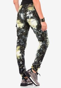 Pantalones cargo ajustados en negro, estampado de tie-dye en amarillo y verde. Con bolsillos, detalles acanalados y una tela texturizada con una silueta ajustada.