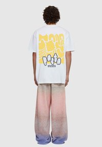 Fehér póló sárga tésztával ellátott grafikával a hátsó részen, széles szárú nadrággal párosítva, amely pinkből lilába átmenő, pöttyös textúrával készült.