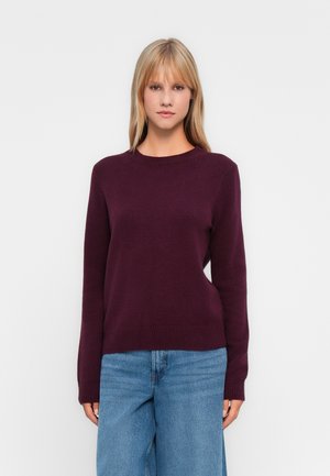 Pull bordeaux avec un col rond, des manches longues et des poignets et un ourlet côtelés. Associé à un jean large taille haute en denim bleu clair.