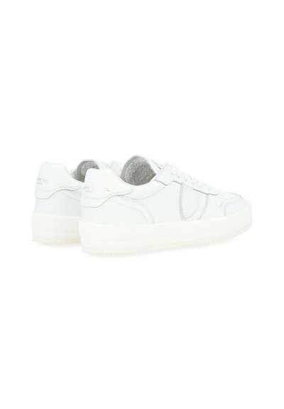 Sneakers bianchi in pelle con una texture liscia, punta rotonda, lacci piatti e una suola in gomma bianca spessa con un branding discreto sul tallone.