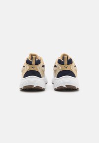 Scarpe da ginnastica beige e blu navy con tessuto in rete, suole bianche imbottite e dettaglio di branding distintivo sul tallone.