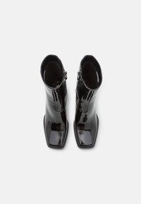 Botines de charol negro hasta el tobillo con punta cuadrada, textura suave, cierre de cremallera y diseño minimalista. Talla 37.