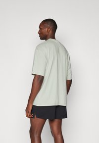 Lys grøn bomulds T-shirt med korte ærmer og en afslappet pasform, båret med sorte shorts. Minimalistisk design, uden synlige mønstre eller grafikker.