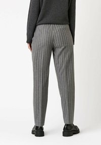 Graue gestreifte Hosen mit geradem Schnitt, mittlerer Taillenhöhe und subtiler Textur. Kombiniert mit schwarzen Schuhen.