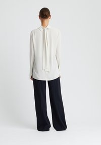 Witte blouse met een strik aan de achterkant, lange mouwen en knoopmanchetten, gecombineerd met losse zwarte broeken. Glad stofgevoel.