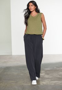 Olivengrøn ærmeløs top med V-hals, kombineret med løse, mørkegrå bukser. Outfit'et har en afslappet pasform og sidelommer. Hvide sneakers.