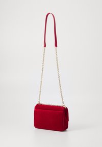 Borsa a tracolla in velluto rosso con una texture liscia, tracolla a catena e forma rettangolare. Presenta una patta superiore e una tasca laterale.