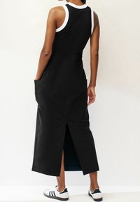 Schwarzes ärmelloses Kleid mit weißem Saum, elastischem Bund, Seitentaschen und Rückenschlitz. Getragen mit weißen und marineblauen Sport-Schuhen.