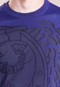 Pull en tricot violet avec un design graphique tonal aux détails complexes, encolure ronde et texture lisse.