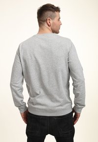 Šedá mikina s dlouhými rukávy, kulatým výstřihem a žebrovanými manžetami. Vyrobena z měkké látky, minimalistický design, ukazující hladkou strukturu.